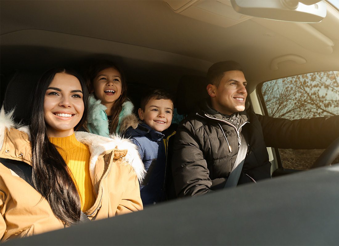 Personal Insurance - Portrait of a Cheerful Family with Two Young Kids Having Fun Driving in the Car on a Road in the Winter on a Sunny Afternoon
